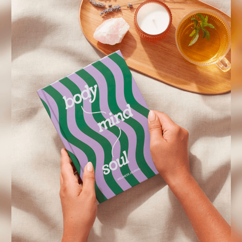 wellness journal body, mind and soul being held along with a tray containing a hot drink and a candle